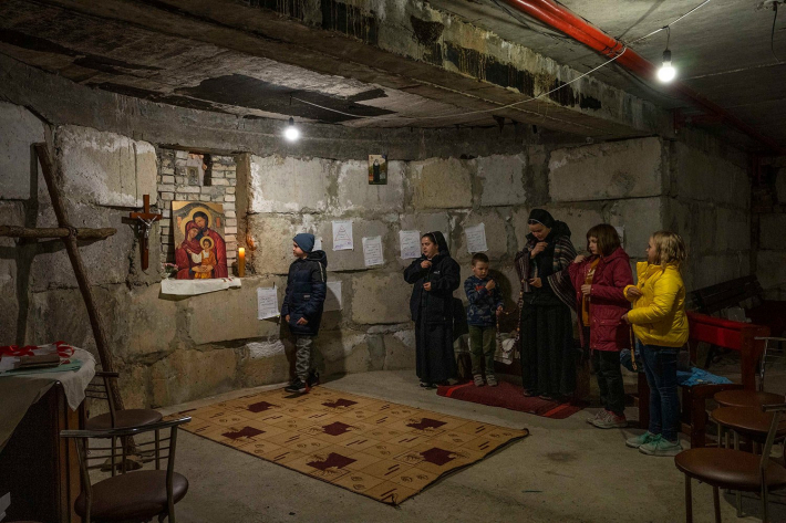 Біженець з Маріуполя 10-річний Ростислав Борисенко, ліворуч, і діти-переселенці моляться з монахинями, у імпровізованій каплиці в бомбосховищі, яке монахині облаштували щоб ховатися під час повітряної тривоги