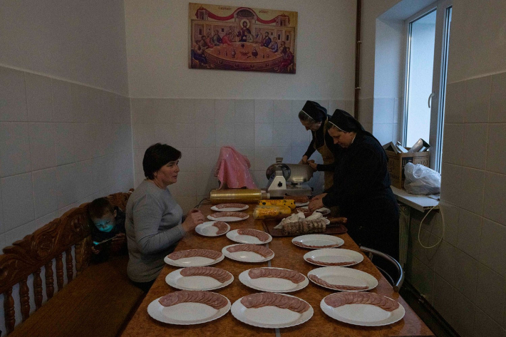 Монахині та внутрішньо переміщена жінка з сином нарізають м’ясо в Гошівському жіночому монастирі, 6 квітня 2022 року