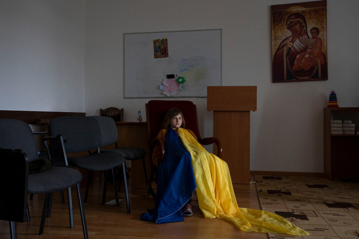 Вимушено переселена дитина, одягнена в імпровізований український прапор, сидить на заняттях із монахинями